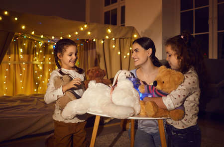 Happy mother playing toy with children daughter at home in dark cozy evening before go to bed....