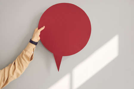 Young anonymous woman or teen girl holding one dark wine red round clean free mockup copyspace speech bubble in hand on gray background. Mock up card for message notification and expressing opinionの写真素材