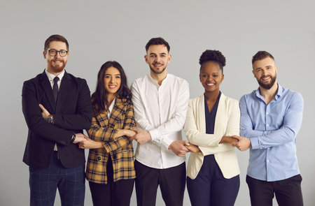 Team of five happy smiling millennial people, startup company coworkers and business partners, standing in row, holding hands and looking at camera. Work community, corporate support, teamwork conceptの写真素材