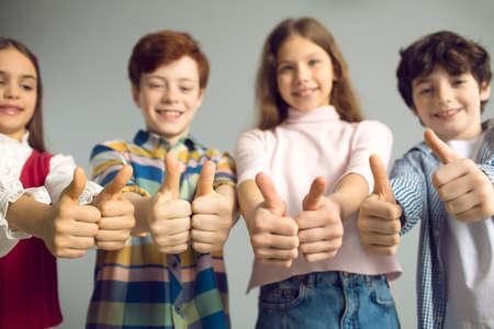 Children giving thumbs up, studio group shot. Happy satisfied junior kids doing like gesture. Primary schoolchildren celebrate success, support good idea, approve of useful suggestion or job well doneの写真素材
