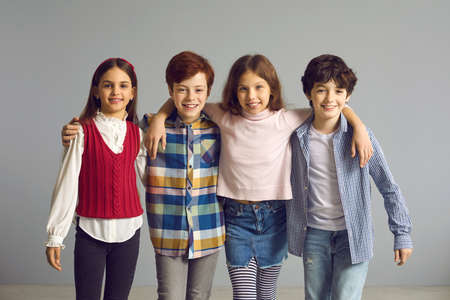 Little boys and girls making friends and having fun together. Happy kids huddling and smiling at camera. Studio group portrait of school children standing in row with arms on each others shouldersの写真素材