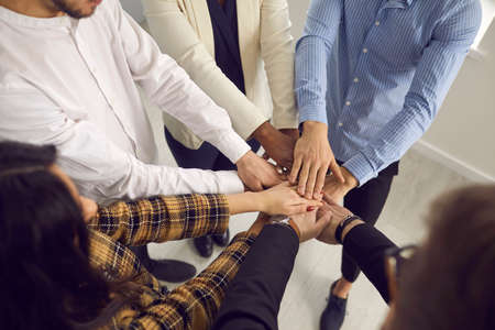 Group of young diverse people putting hands together. Confident business team joining hands in...
