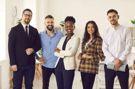 Group of five millennial people in office suits smiling and looking at camera. Portrait of confident...