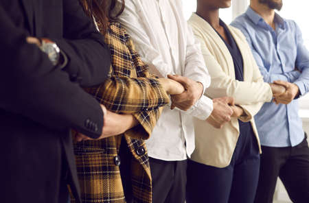 Cropped shot of diverse business team standing together holding hands. United young Caucasian and African American people and coworkers supporting each other. Teamwork and strong work community conceptsの写真素材