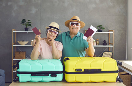 Elderly couple in love. Portrait of a cheerful senior couple leaning on suitcases holding passports and tickets. Active elderly man and woman going on summer vacation. Traveling and honeymoon concept.の写真素材