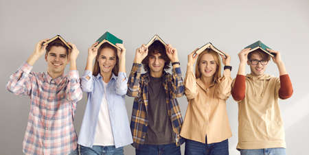 Group of happy college or university students holding books on head like house roof tops, smiling and looking at camera. Concept of education and having fun while studyingの写真素材