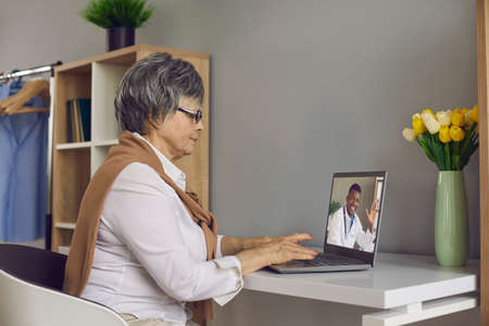 Telemedicine, telehealth, ehealth, remote healthcare service, medical advice online, social medicine concept. Elderly grey-haired woman having virtual consultation doctor on laptop sit at homeの写真素材