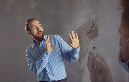 adult man waves his arms, feeling great fear of being injected with the vaccine against Covid-19. Man is afraid of doctors mistakes and therefore refuses to be vaccinated. Gray background. Banner.の写真素材