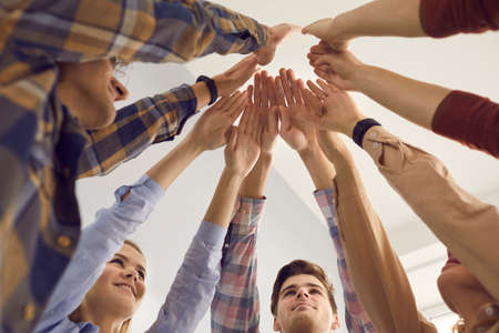 Bottom view young men and women raise their hands and join them standing in a circle. Concept of...