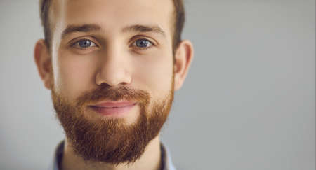 Closeup portrait of happy confident young man looking at camera with friendly positive face expression on gray studio background. Copy space banner with head shot for clients testimonialの写真素材