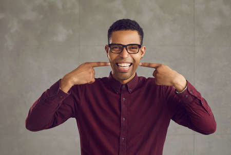 Confident happy smiling young african american man pointing with both forefinger to white teeth...