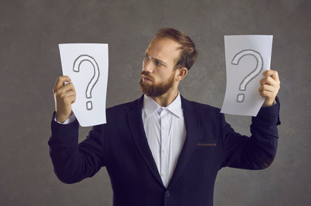 Man holding  papers with question mark symbols, thinking, unsure, trying to make choice between different business options, asking himself what decision to takeの写真素材