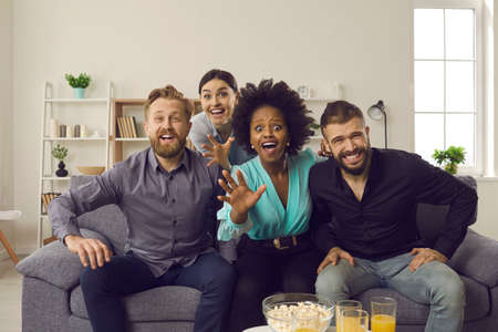 Group of scared international friends are sitting at home on the couch and watching a horror movie...