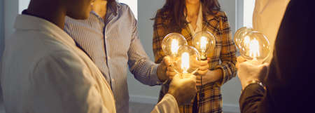 Group of happy young multiracial business people holding electric light bulbs. Team of colleagues join Edison light bulbs as conceptual metaphor for teamwork and sharing ideas in creative communityの写真素材