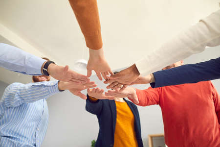 Team of happy business people put hands together. Group of teammates standing in circle join hands showing unity and motivation to reach success. Crop low angle shot, view from below. Teamwork conceptの写真素材