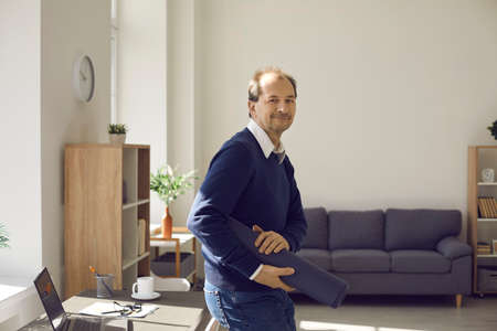 Portrait of smiling senior adult man employee walking with yoga mat for exercise. Balance between...