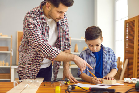 Father teaching son to build wooden house using hand tools and wooden plank at home carpentry and joinery workshop. Dad and boy child working together make toy for school DIY projectの写真素材