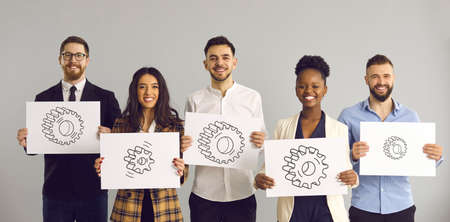 Group portrait of happy smiling multiethnic people, business team members and colleagues, holding paper sheets with pictures of different gears standing isolated on white background. Teamwork conceptの写真素材