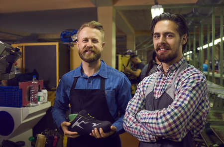Portrait of sports footwear factory workers with their brand new product. Two happy young men...