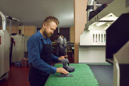 Skilled factory worker making new shoes. Side view of young man standing at table in workshop and working with shoe detail patterns. Footwear manufacturing industry conceptの写真素材
