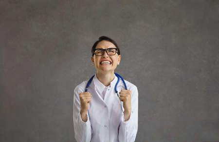 Excited young female doctor standing with yes closed and clenched fists showing gesture winner. Studio shot face portrait. Victory, success and achievement in health healthcare medicine conceptの写真素材