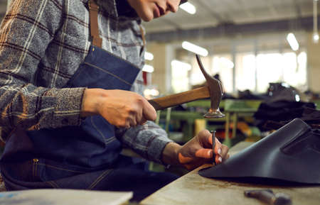 Shoe factory worker using professional tools. Cropped shot woman sitting at workshop table using...