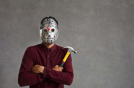 Studio portrait of an unknown man on a gray background who is dressed in a spooky maniac mask....
