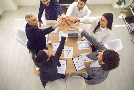 Well done. View from above of group of business people standing around office table and giving each...