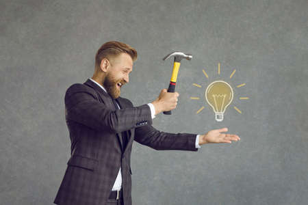 Side profile view of young company executive in smart suit breaking yellow light bulb doodle with hammer. Concept of looking for breakthrough ideas and finding successful innovative business solutionsの写真素材