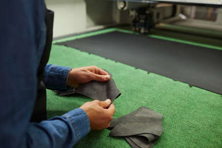 Closeup shot of experienced shoemaker hands working with material pieces. Cobbler preparing leather for shoe making skin patterns. Workflow process. Cropped image. Footwear manufactory industryの写真素材