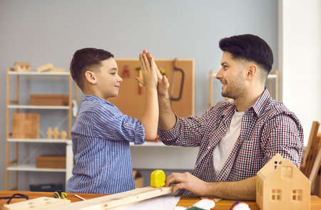 Happy smiling father giving high five and support to cheerful son after successful building work...