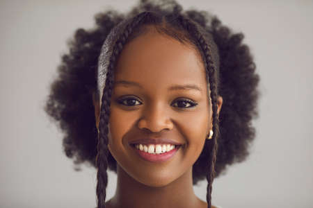 Young African American teenager girl student with curly fashion hairstyle smiling looking at camera closeup face portrait on grey studio background. Good mood, positive emotion and youth conceptの写真素材
