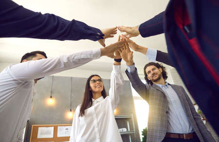 Diverse business team partners joining hands together standing in office. Teamwork and collaboration, unity and support concept. Cooperate motivation and inspiration idea. Shot with view from bottomの写真素材