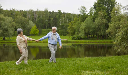 Happy senior couple having a good time together. Old man and woman walking in a green park on a fine...