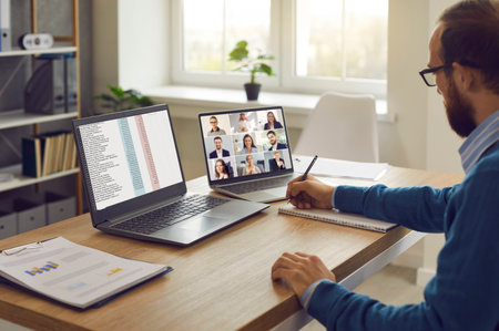 Corporate team manager sitting at table with two laptop computers having online conference with employees and coworkers. Virtual meetings, remote teamwork, telework and business management conceptsの写真素材