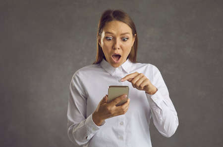 Woman looks at smartphone screen with surprised shocked astonished face expression. Lucky lady...