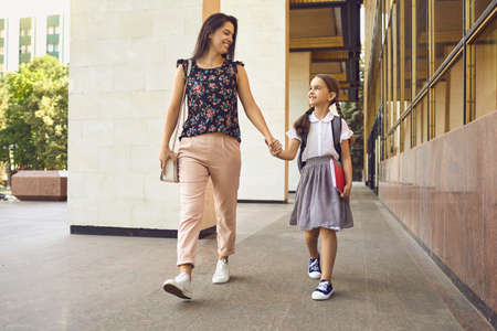 Smiling mother and child with a backpack go to school cheerfully. Education training learning for...