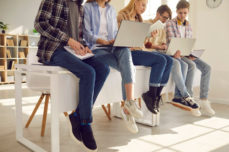 Middle section teenager secondary or high school student studying using laptop and paper copy-book, notebook sitting on classroom desk. Teen pupils involved in learning process working togetherの写真素材