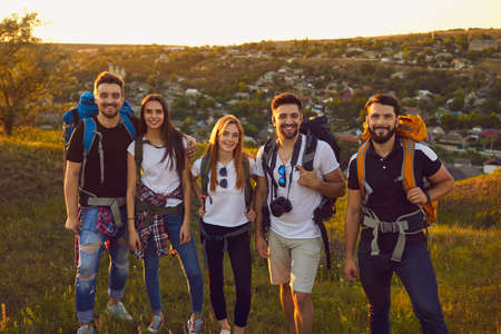 Portrait of young friends with rucksacks looking at camera in mountains. Team of millennial tourists hiking outdoors in summertimeの写真素材