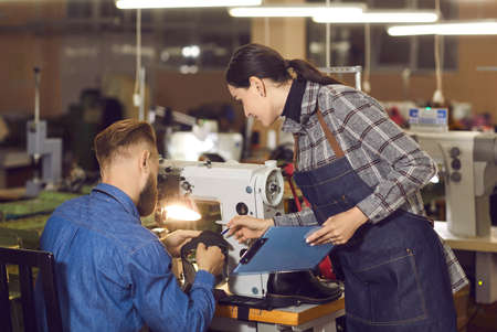 Female quality control manager talking to shoemaker sewing leather working at workplace. Woman...