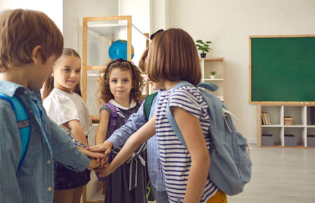 Team of elementary school children joining hands standing in circle in modern classroom. Group of...