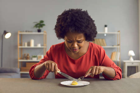 Young lady having tiny serving for lunch. Sad black woman whos sticking to strict diet eating nothing more than ridiculous portion of one little piece of apple. Nourishment and weight loss conceptの写真素材