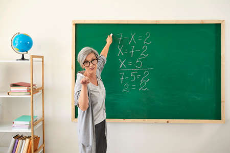 School education. Senior female teacher explaining new material near blackboard at clasroom, copy space. Mature professor giving lecture onlineの写真素材