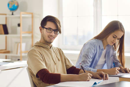 Portrait of high school university male teenager student looking at camera while writing paper...