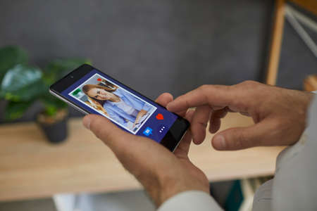 Dating online. Man looks through a photo of a young european woman on his smartphone, clicks I like...
