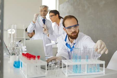 Serious male scientist, doctor or lab technician in protective goggles and gloves doing medical...