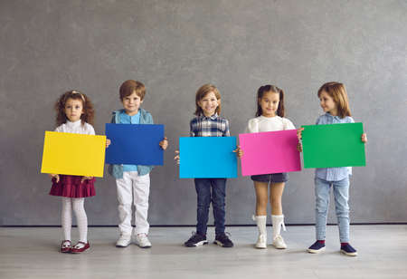 Diverse children group standing in row holding empty blank color poster or placard speech bubble ready for advertising text. Smiling preschool kids or primary school children portrait on studio spaceの写真素材