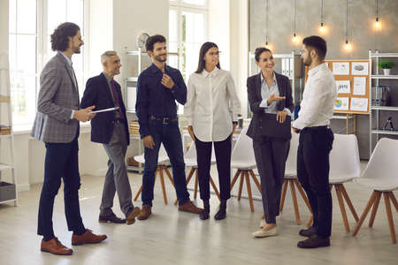 Smiling various office workers have a pleasant conversation at a meeting in the office. People of all ages work with each other in a comfortable and positive atmosphere. Concept of successful teamworkの写真素材