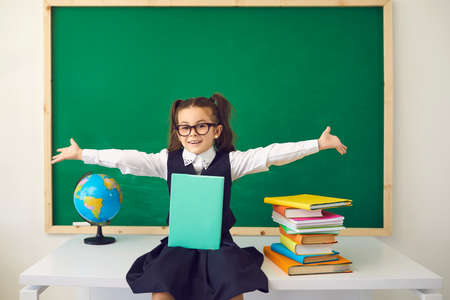 Back to school concept. Schoolgirl with glasses smiling in classroom with a school blackboard....