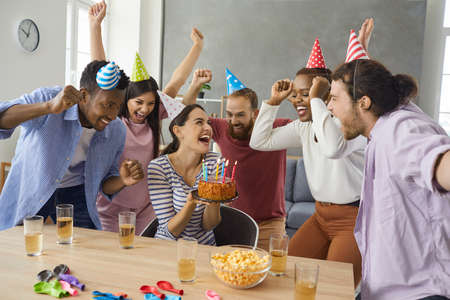 Multinational friends are celebrating a birthday at a friends house, having fun, cake with candles,...